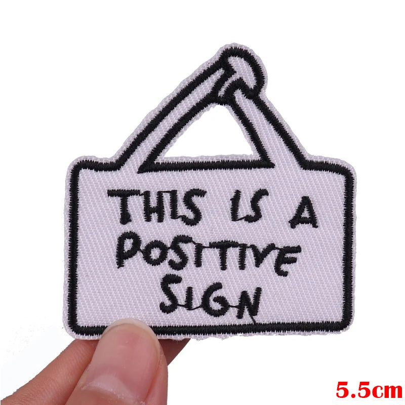 A white embroidered patch with black text that reads This is a positive sign