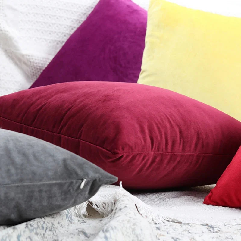 A collection of velvet throw pillows in shades of purple, yellow, and deep red resting on a white textured surface.