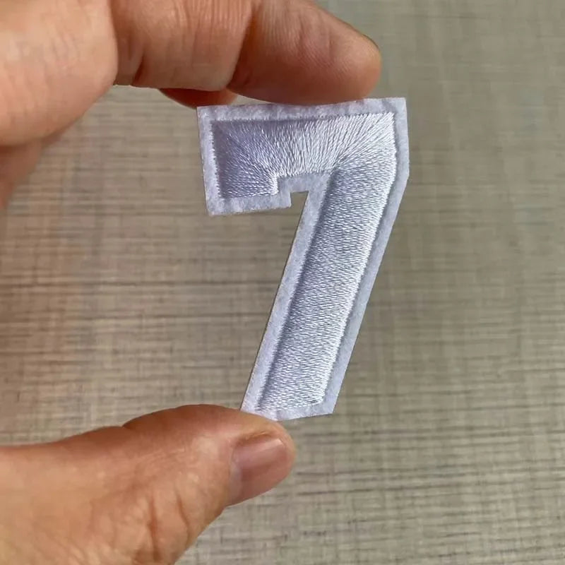 A hand holds a white embroidered number 7 patch for apparel.