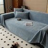 A light blue minimalist herribone chenille sofa cover draped over a sofa with throw pillows and a decorative cloth.