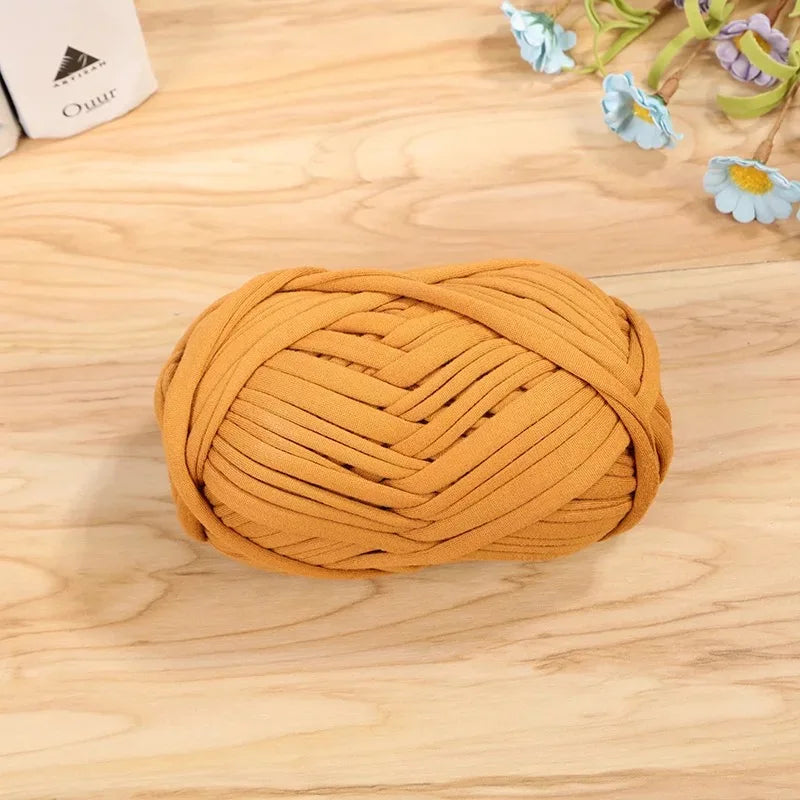A ball of mustard yellow flat thread yarn for crafting and sewing resting on a light wooden surface.