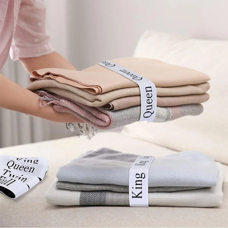 A set of four elastic bed sheet organizer straps in various shades of beige and gray are shown on a white surface.