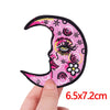 Pink crescent moon embroidered iron-on patch with floral and eye designs being held by a hand
