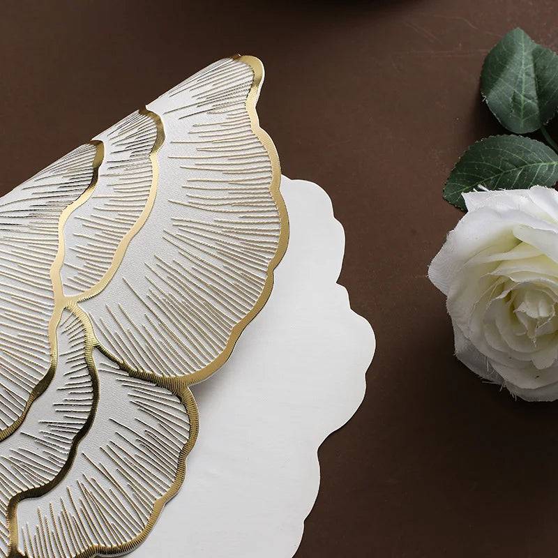 Gold plated peony coasters with textured leaves resting on a brown surface next to a white rose.