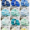A collection of satin craft ribbons in various colors including beige, gold, pink, green, and brown rolled for decorative tri
