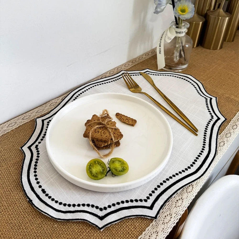 A white ceramic plate with a gold fork and knife is set on an embroidered cotton linen placemat.