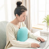 A woman is using a laptop while resting her head on a light blue memory foam neck and travel pillow.