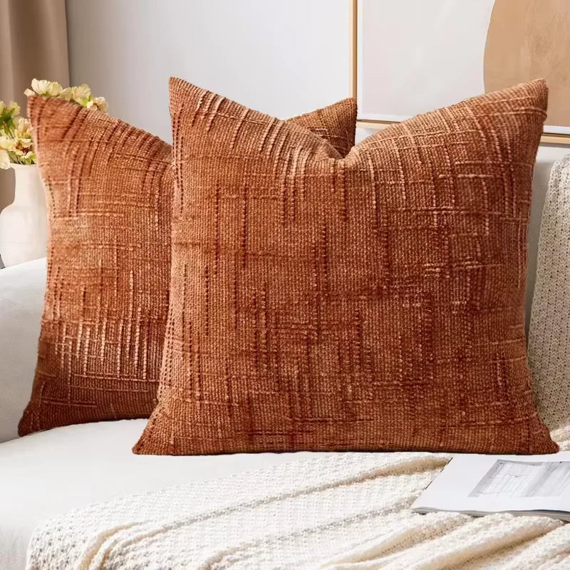 A close-up of a textured, rust-colored boucle throw pillow resting on a white surface.