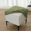 A light green geometric jacquard ottoman slipcover draped over a white upholstered ottoman.