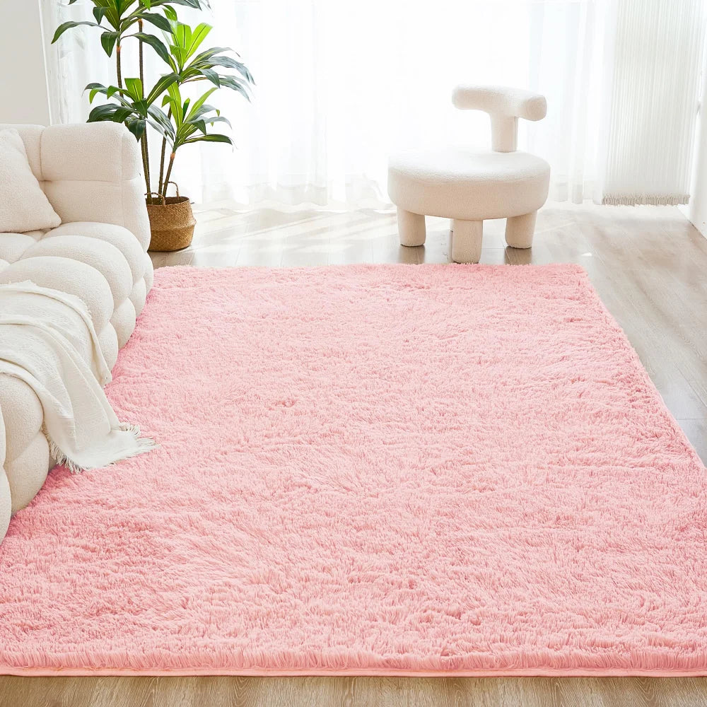 A pink shaggy rug is placed on a light wooden floor in a bright room with a white stool and green plants.