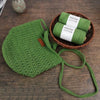 A hand-knitted green mesh face mask is displayed next to a basket of rolled green cotton yarn.