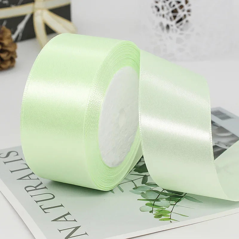 Roll of light green satin craft ribbon with white filling shown next to a product packaging card
