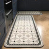 A rectangular gray and black anti-slip floor mat placed on a light wood floor in a kitchen or entrance area.