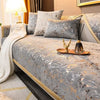 A luxurious bed with a gray velvet cover, white pillows, and gold accents in a bedroom setting.