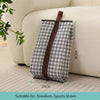 A gray and white patterned portable boot storage bag with a brown carry handle resting on a light-colored sofa.
