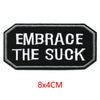 Black embroidered patch with white text that reads Embrace the Suck