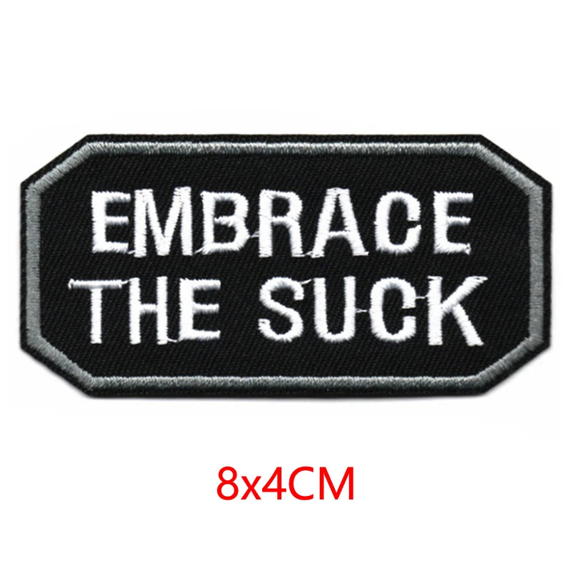 Black embroidered patch with white text that reads Embrace the Suck