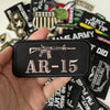 A hand holds a black iron-on patch featuring the text AR-15 and an assault rifle silhouette.