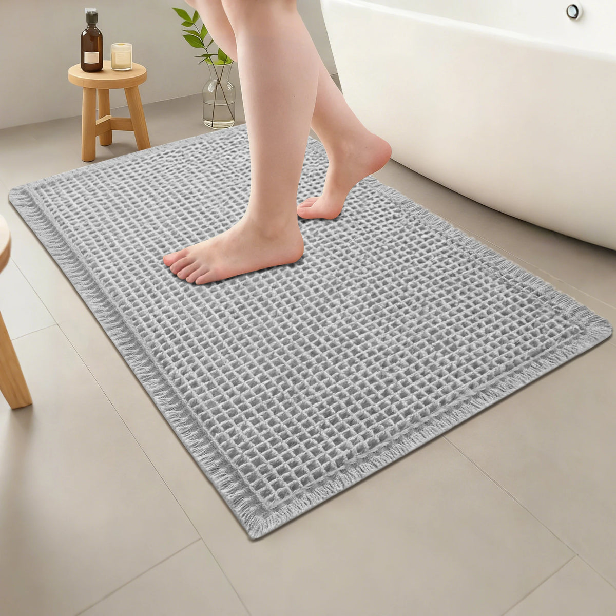 A person's feet standing on a gray waffle design non-slip bathroom mat on a tiled floor.