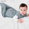 A baby wearing a light blue patterned cotton sleep sack lying on white bedding.