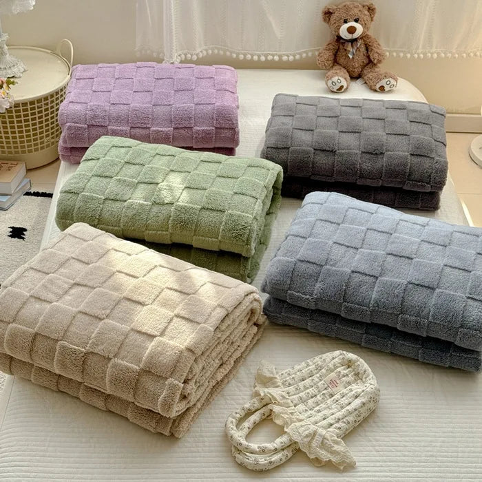 A collection of folded checkered fleece throw blankets in purple, green, gray, and beige are displayed on a white surface.
