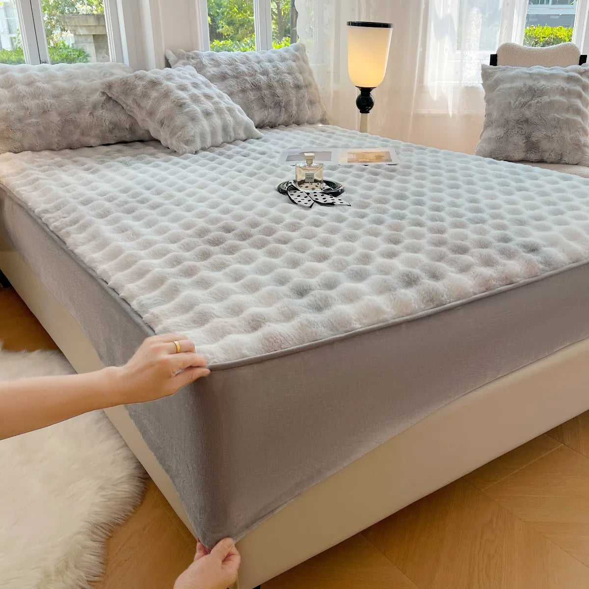 A luxury faux rabbit fur fitted sheet set is displayed on a bed with light gray bedding and white curtains.