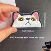 A white cat face patch with pink ears and yellow eyes is being held against a dark background.
