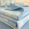 A stack of light blue and white floral quilted bedspreads and pillows on a bed.
