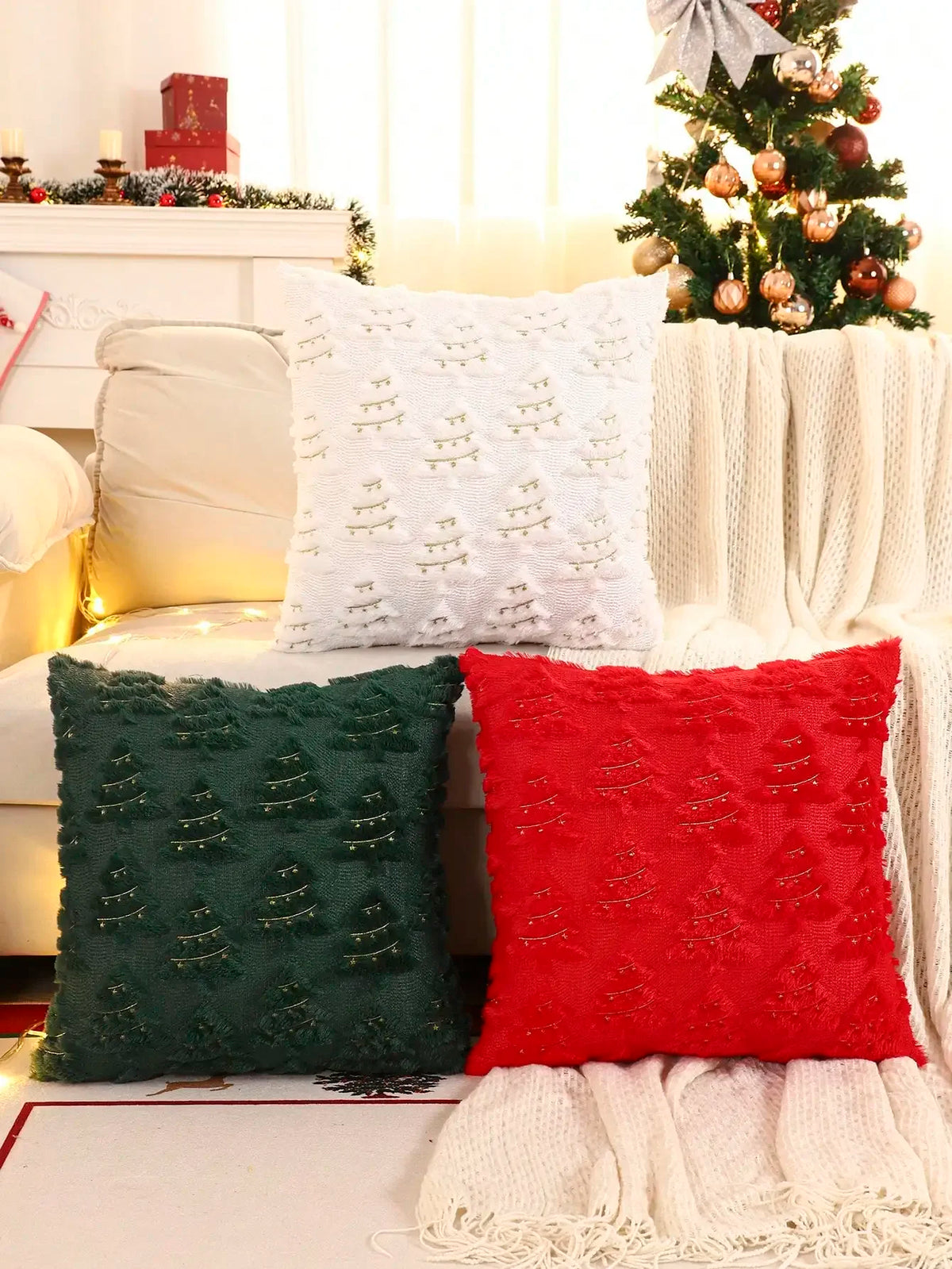 A set of three textured throw pillows in white, dark green, and red velvet are displayed on a white sofa.