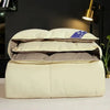 A stack of cream-colored goose down comforters or duvets resting on a white surface.