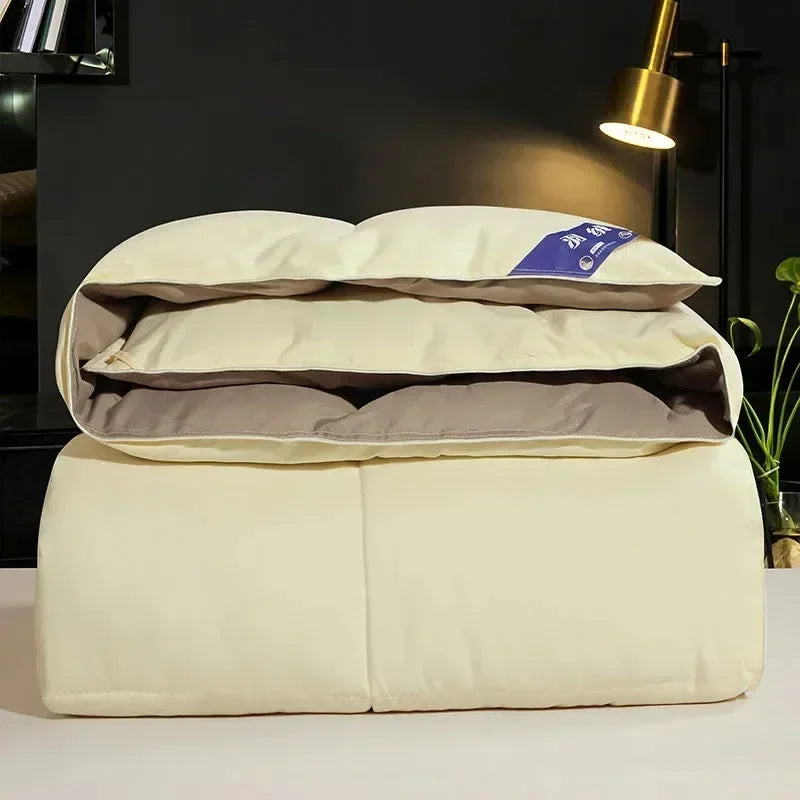 A stack of cream-colored goose down comforters or duvets resting on a white surface.