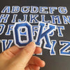 A hand holds an embroidery patch of the letter O and K from a set of alphabet iron-on patches.