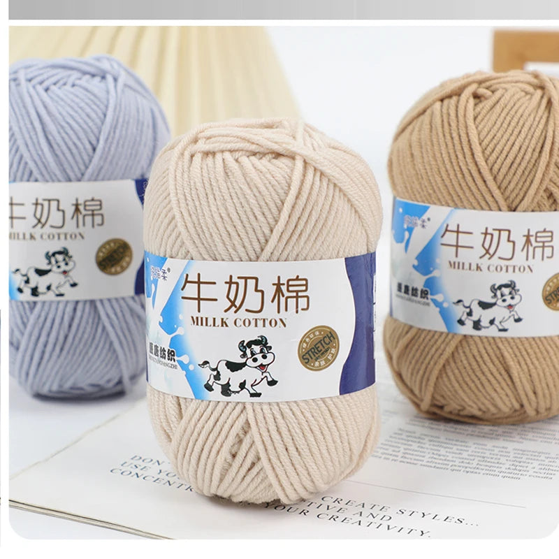 A close-up of skeins of light blue and beige milk cotton yarn for knitting displayed on a white background.