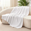 A white ultra-soft 100% cotton gauze blanket draped over a light-colored sofa.