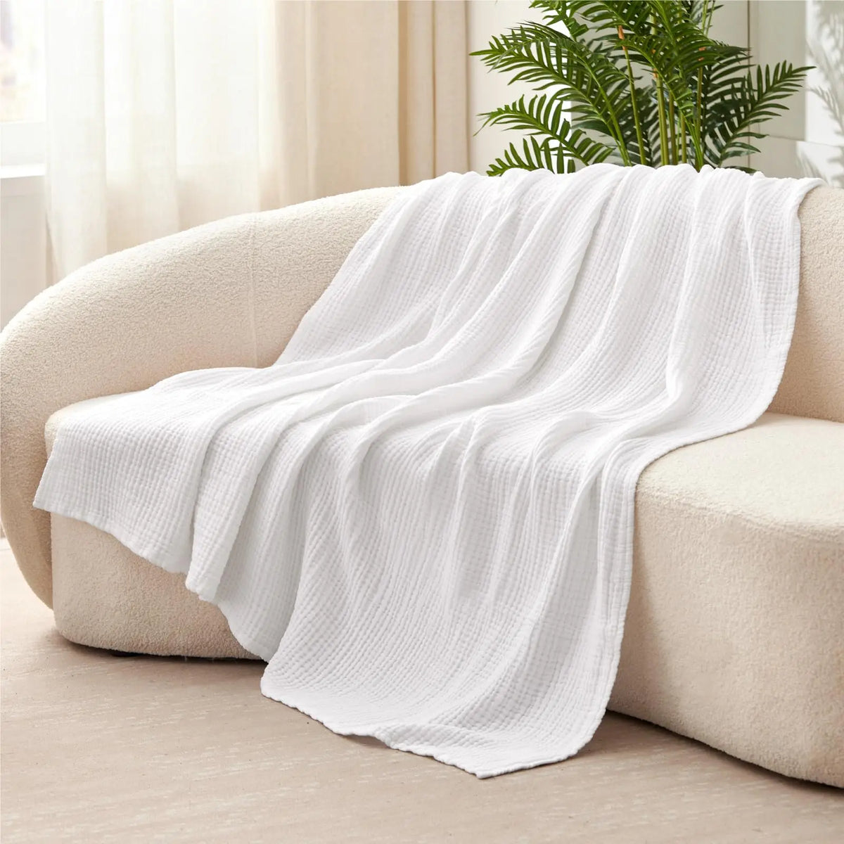 A white ultra-soft 100% cotton gauze blanket draped over a light-colored sofa.