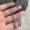 A hand is holding several strands of dark gray hand-woven wool and linen blended yarn against a textured background.