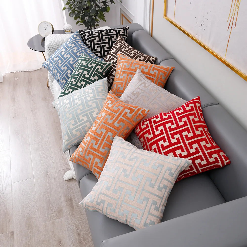 A collection of geometric patterned lumbar pillows in shades of orange, gray, and white on a gray sofa.