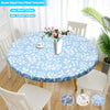 Light blue floral patterned round vinyl tablecloth set with white dining chairs and a potted plant
