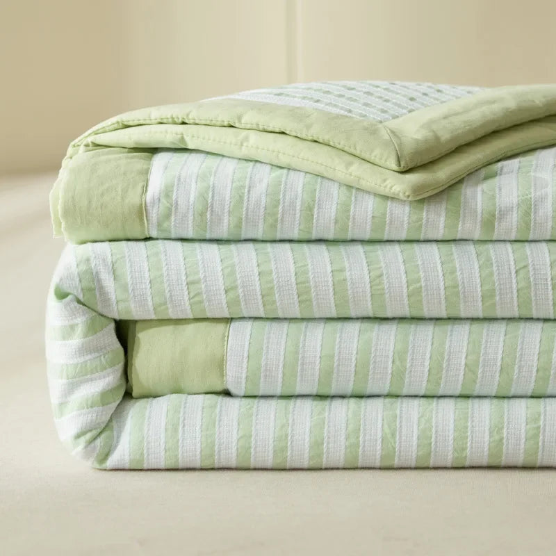 A stack of light green and white striped luxury jacquard summer quilts.