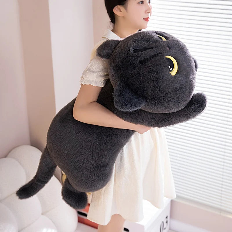 A woman is holding a dark gray black cat plush pillow in front of a window.