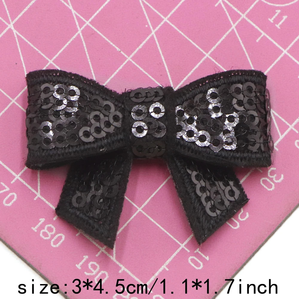 Black and silver sequin bow patches for DIY decoration shown on a pink grid background