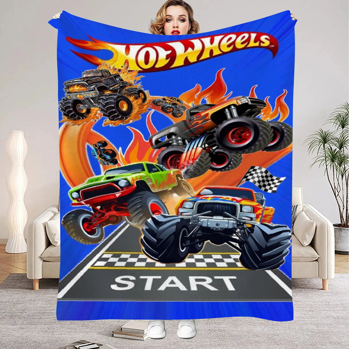 A colorful flannel throw blanket featuring Hot Wheels monster truck graphics and text on a blue background.