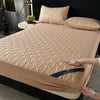 A beige quilted mattress protector is shown on a bed, with a hand adjusting the fabric.