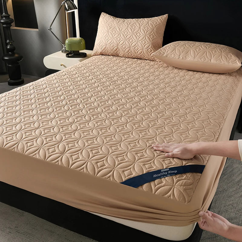 A beige quilted mattress protector is shown on a bed, with a hand adjusting the fabric.