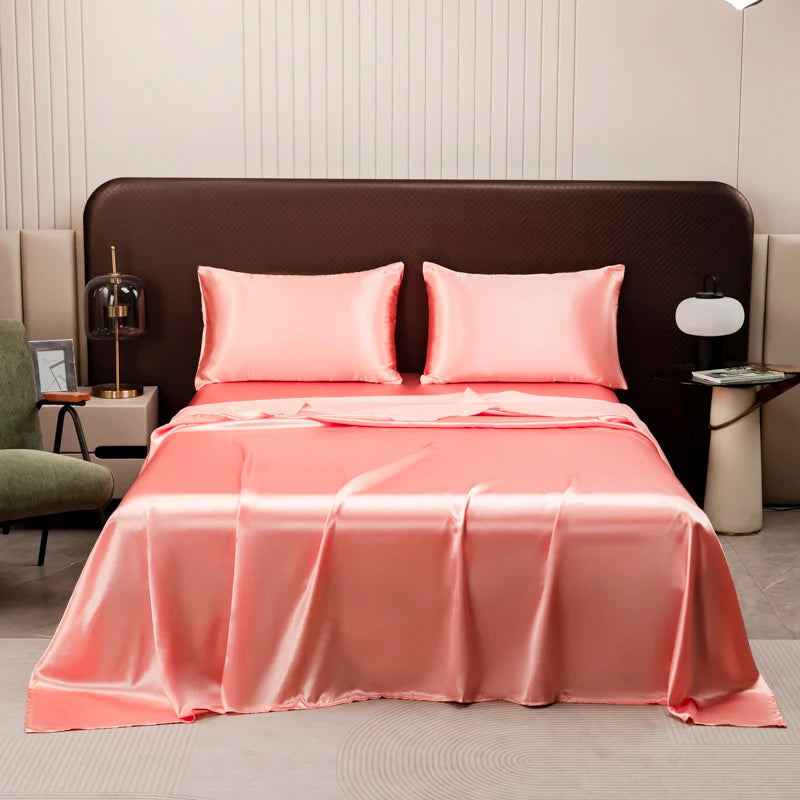 A pink satin flat bed sheet set is displayed on a bed with a brown headboard.