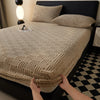 A person is adjusting a beige plush jacquard mattress cover on a dark bed.