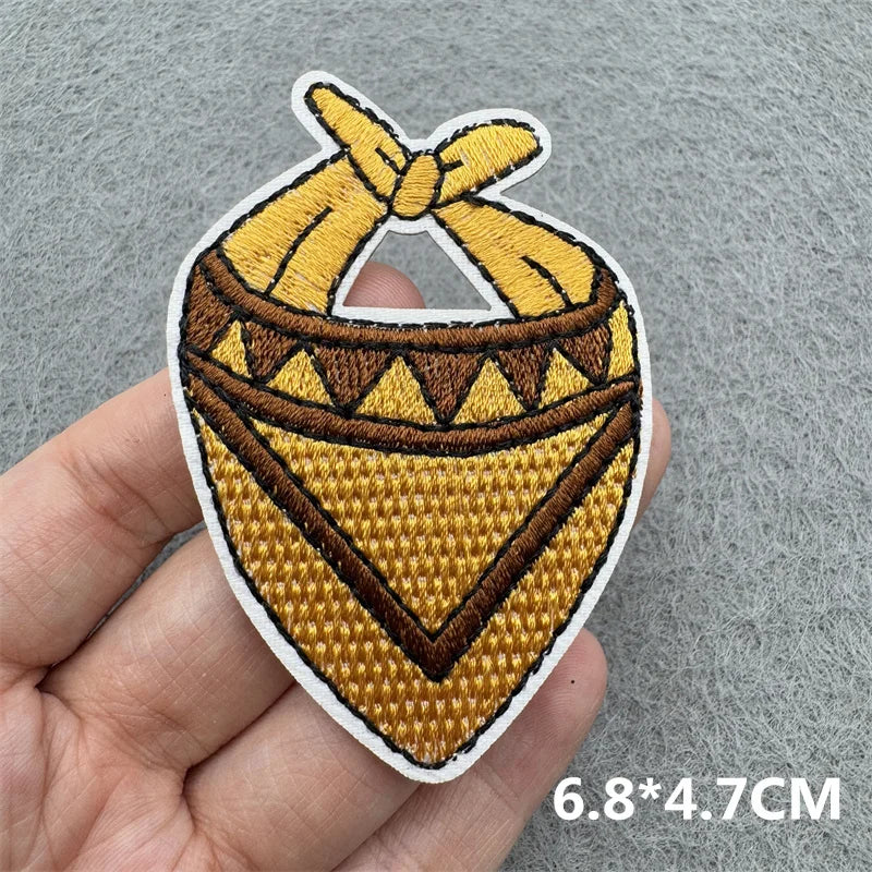 A yellow and brown embroidered patch shaped like a cowboy hat, shown being held in a hand.