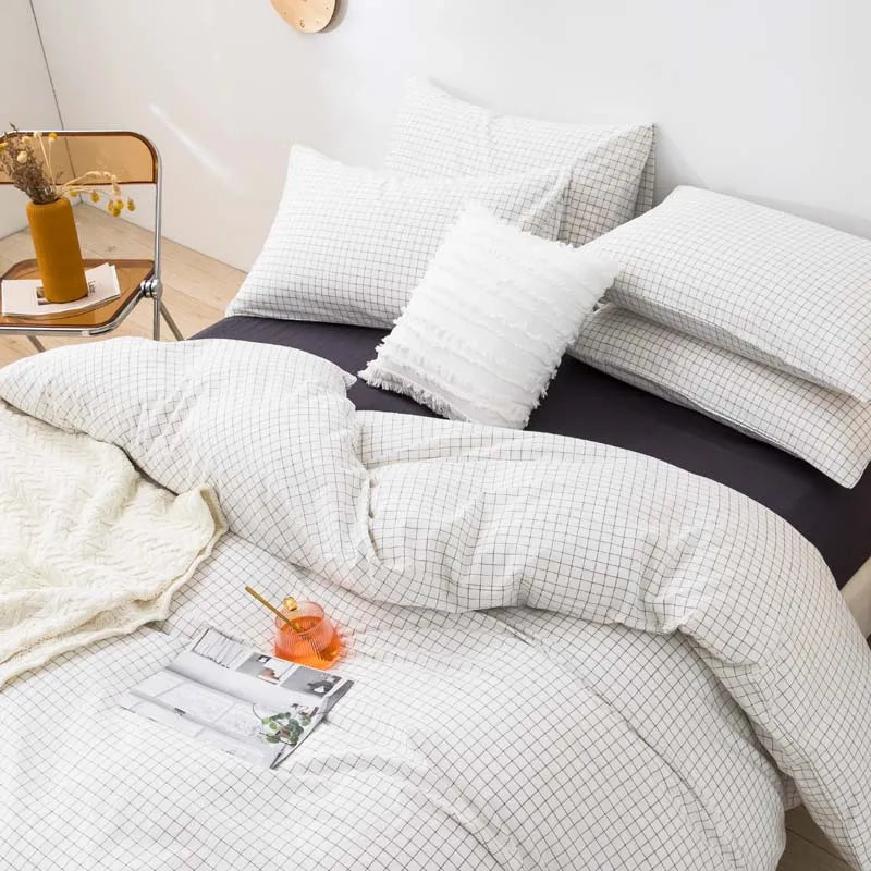 A set of three white plaid duvet covers and pillowcases displayed on a dark bed.
