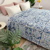 A blue and white patterned embroidered cotton quilted bedspread on a bed with pink pillows and green plants.