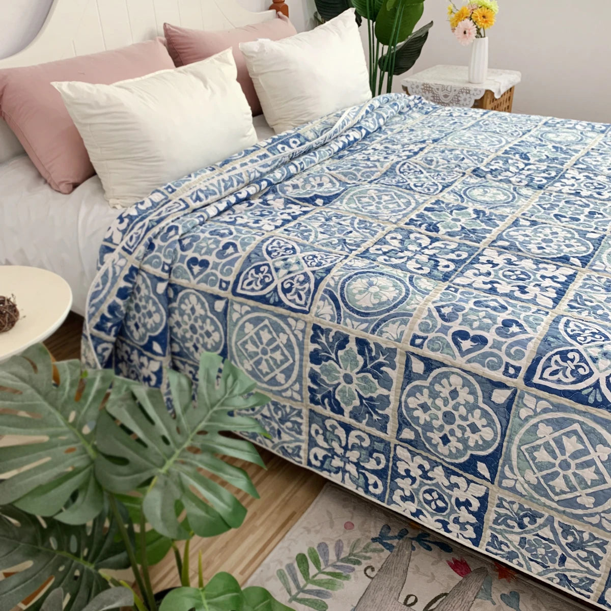 A blue and white patterned embroidered cotton quilted bedspread on a bed with pink pillows and green plants.